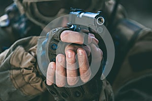 The soldier in the performance of tasks in camouflage and protective gloves holding a pistol