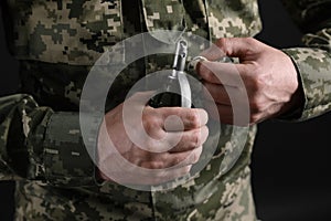 Soldier pulling safety pin out of hand grenade on black background, closeup. Military service