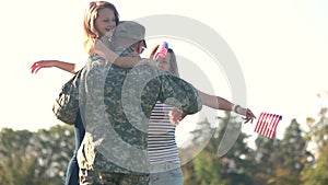 Soldier reunited with his family on a sunny day in the park.