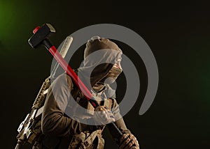 A soldier-saboteur rebel in military clothing with a weapon on a dark background holding a sledgehammer