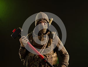 A soldier-saboteur rebel in military clothing with a weapon on a dark background holding a sledgehammer