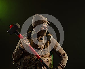 A soldier-saboteur rebel in military clothing with a weapon on a dark background holding a sledgehammer