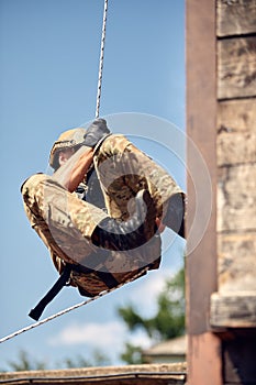 Soldier training rappel with rope. Military man does hanging on climbing equipment