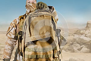 Soldier in uniform holding backpack on desert background