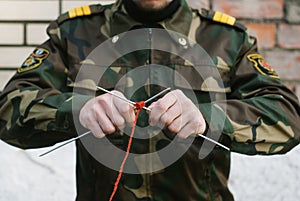 A soldier in uniform knits with needles and red thread