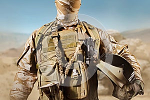 Soldier in uniform standing in desert background with helmet