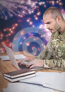 Soldier using a laptop with a fireworks in background