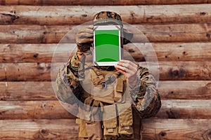 Soldier using tablet computer against old wooden wall in military camp to stay in contact with friends and family