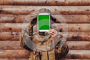 Soldier using tablet computer against old wooden wall in military camp to stay in contact with friends and family