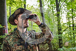 Soldier looking through binoculars while patrolling in forest