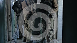 Soldiers in camouflage with combat weapons sneak along the corridors of the old building, the military concept