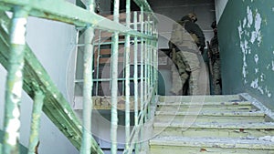 Soldiers in camouflage with combat weapons sneak along the corridors of the old building, the military concept