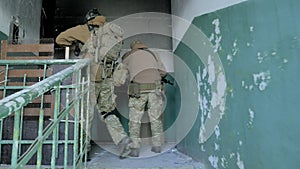 Soldiers in camouflage with combat weapons sneak along the corridors of the old building, the military concept