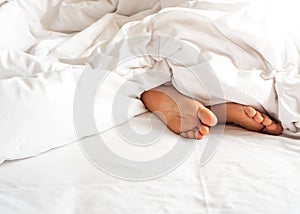 Sole of woman foot in messy blanket on bed. White pillow with bl