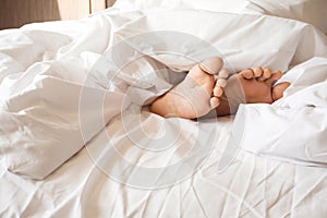 Sole of woman foot in messy blanket on bed. White pillow and blanket.