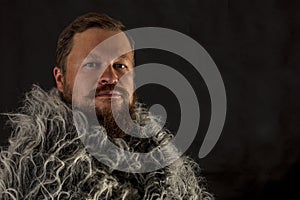 Solid bearded man in a fur mantle studio portrait