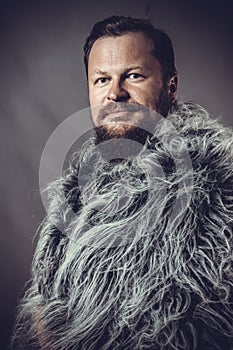 Solid bearded man in a fur mantle studio portrait