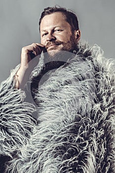 Solid bearded man in a fur mantle studio portrait