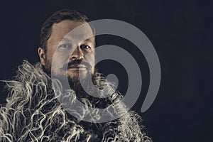 Solid bearded man in a fur mantle studio portrait