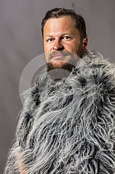 Solid bearded man in a fur mantle studio portrait