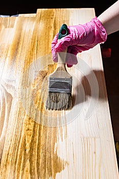 Solid board is hued with wood stain by paintbrush