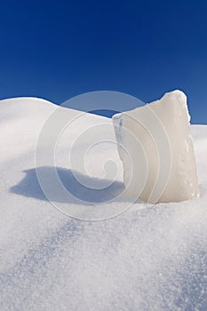 Solid ice cube, snowdrift and cloudless blue sky