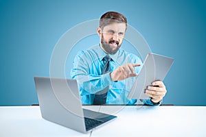 Solid man in an office at a computer holds a tablet in one hand and clicks on it when performing financial reports