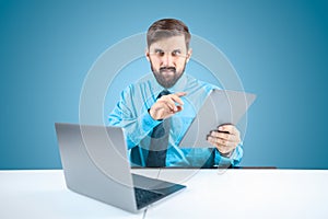 Solid man in an office at a computer holds a tablet in one hand and clicks on it when performing financial reports