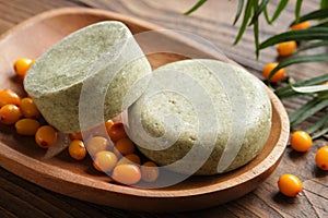 Solid shampoo pieces with sea buckthorn berries extract or homemade natural organic soap bars on wooden soap dish.