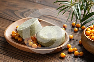 Solid shampoo pieces with sea buckthorn berries extract or homemade organic soap bars on wooden soap dish.