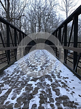 A SOLID WOODEN BRIDGE GUIDES HIKERS ALONG A SNOWY TRAIL IN A PUBLIC PARK