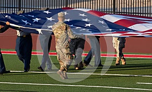 Solider in camouflage caring large American flag on field before a football game