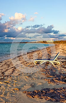 Solitary beach bed, ocean, evening sky, clouds, sea grass on sandy shore Cuba photo