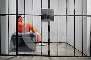 Solitary cell with a criminal in an orange robe in an asian prison. Copy space. Sad emotions of a young guy.