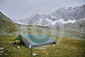 Solitary green tent set up on a rocky terrain against the backdrop of towering snow-capped mountains