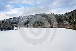 Solitary hotel building in a beautiful snowy winter landscape with forest and frozen dam