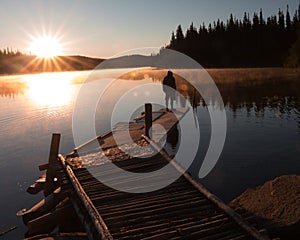 Solitary Man Standing On A Dock On A Lake With Sun Setting