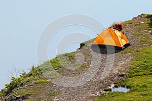 Solitary orange tent camped near water edge