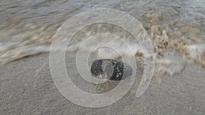 Solitary stone in the sand on the shorebreak