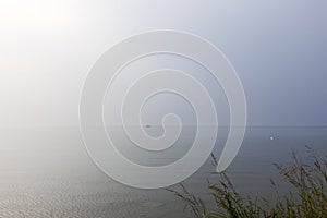 A solitary swan and a lone fishing boat are adrift on Lake Garda vast waters, encapsulated by the ethereal beauty of a foggy