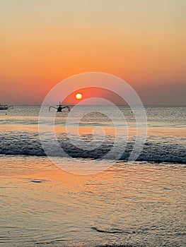 Solitary vessel floating in a peaceful sea at sunset with an orange sky