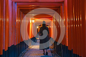 Solitary Wanderer in Traditional Japanese Torii Gates Tunnel at Dusk