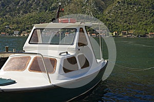 A solitary white boat floats on the calm waters of Kotor Bay, the majestic backdrop of rugged mountains under a blue sky