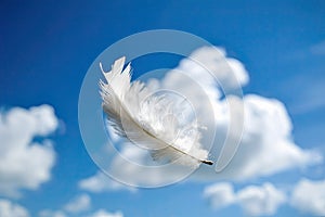 Solitary white fluffy feather floating against a cloudy blue sky background