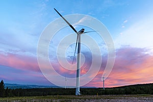 Solitary wind turbine at sunset, summertime, red clouds on horizon, blue sky.