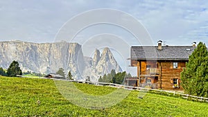 A solitary wooden house, crowns a lush hill with the majestic Mt. Schlern forming a regal backdrop