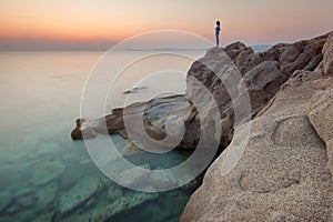 Solitude girl watching sunrise high up on cliff by sea