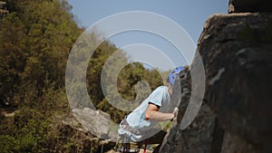 Solo climber in blue ascending a cliff side with focused intent amidst verdant nature.