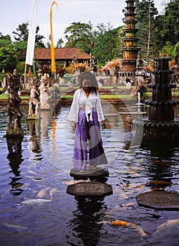 Solo Female Traveler Walking on Stepping Stones around Koi Fish at Main fountain at Tirta Gangga, Bali