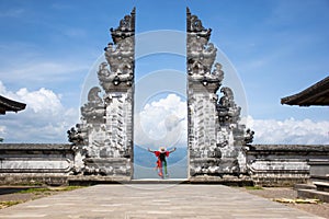 A solo tourist taking photos in Hindu temple heaven`s gate wearing colourful Sarong with blue background sky in Bali